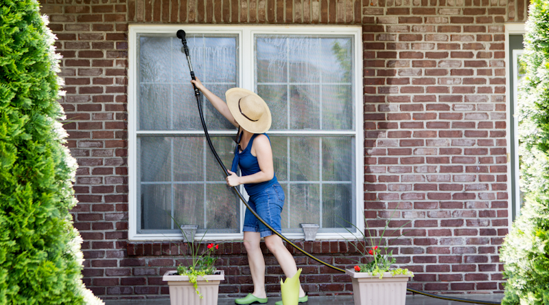 Photo of a woman washing the window frames on a house. Photo from Adobe Stock.