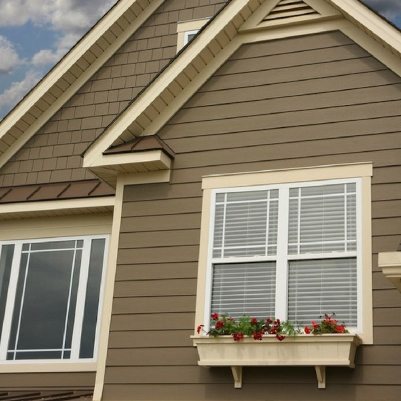Cream-colored trim around white windows with prairie grids on home with brown siding exterior