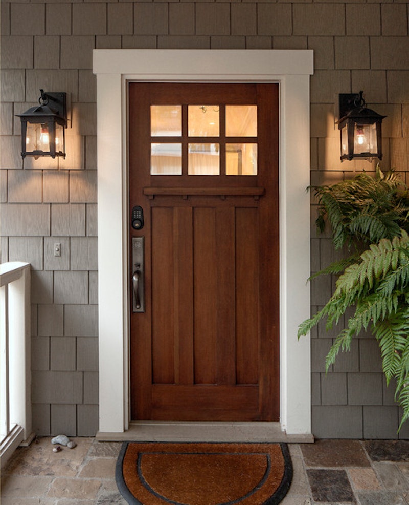 Woodgrain front door with metal hardware, white trim, and gray shake siding