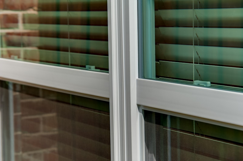 Close up of light colored single hung windows with blinds visible through the glass.