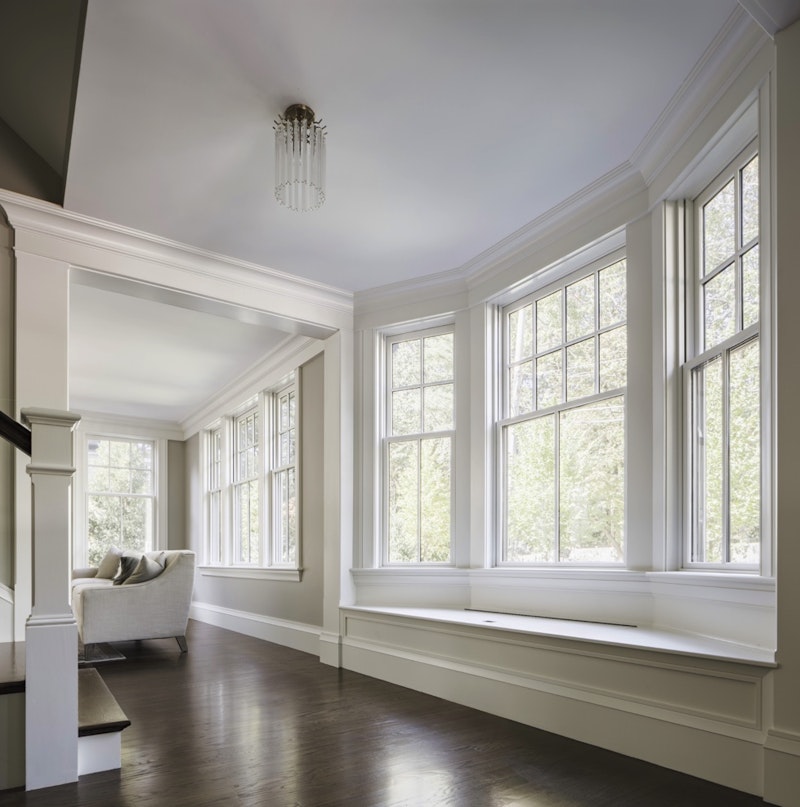 Interior of a foyer and stairs and white three lite, single-hung bay windows with grids. 