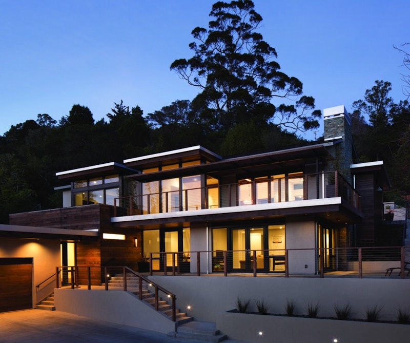 Large contemporary stucco and wood home surrounded by pine trees and illuminated EpicVue windows.